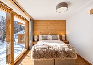 Een moderne slaapkamer met een houten hoofdbord, een groot bed met zachte beddengoed en uitzicht op een besneeerd landschap door een glazen deur.