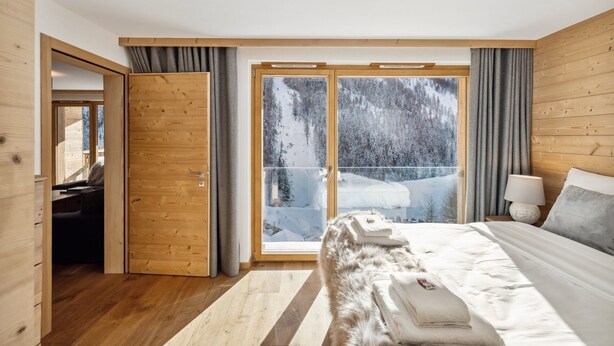Un dormitorio moderno con una cama grande, paredes de madera y un ventanal corredero que da a un área exterior nevada.