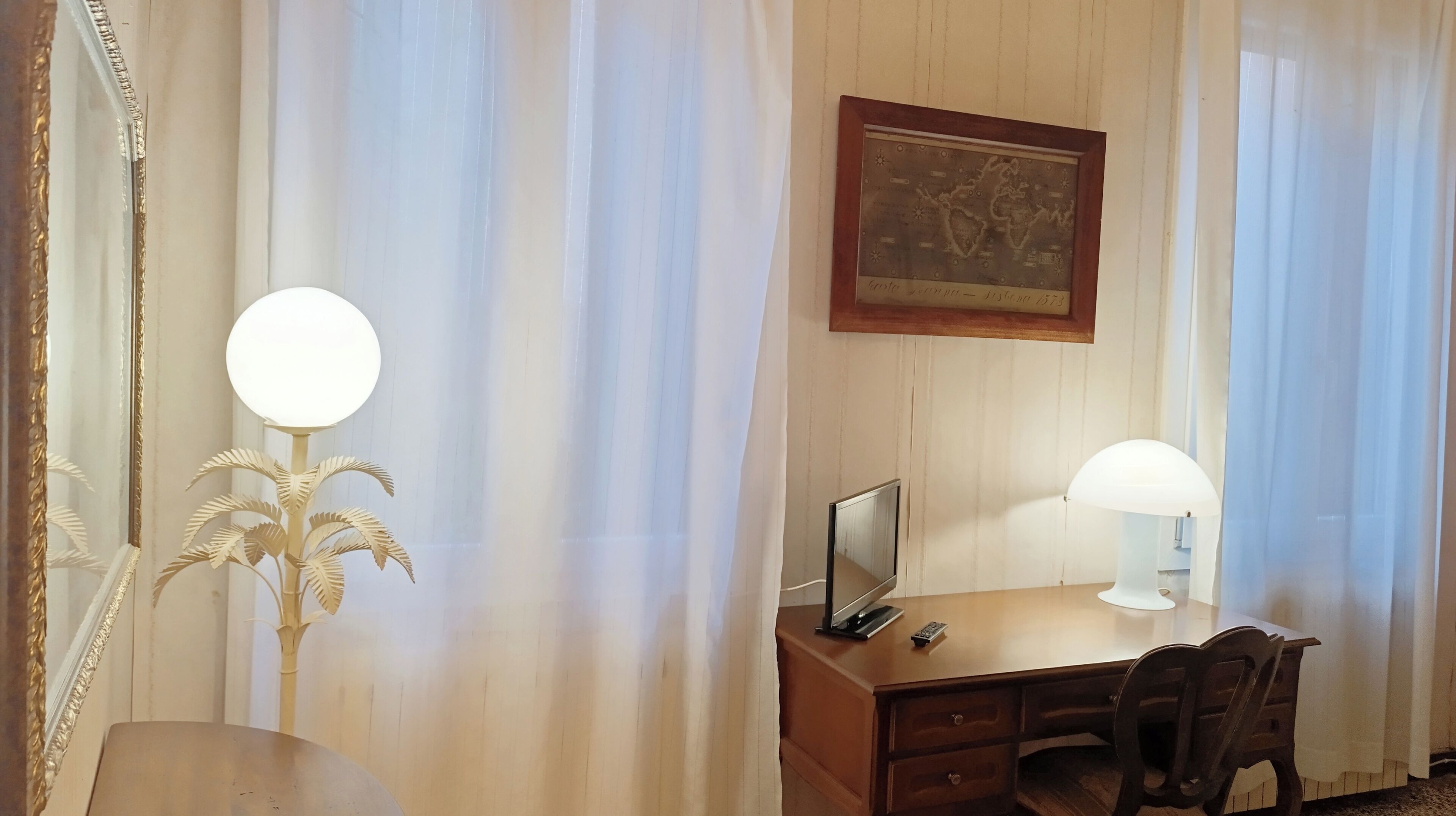 Une chambre d’hôtel équipée d’un bureau, d’une chaise, de deux lampes, d’un tableau encadré au mur et de rideaux légers.