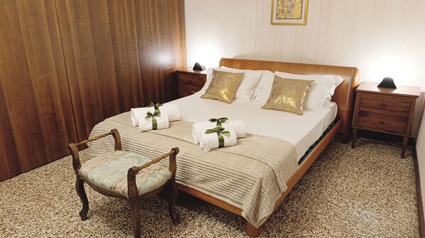 Una cama bien hecha con almohadas, una mesita de noche con lámpara, una silla y suelo de madera.