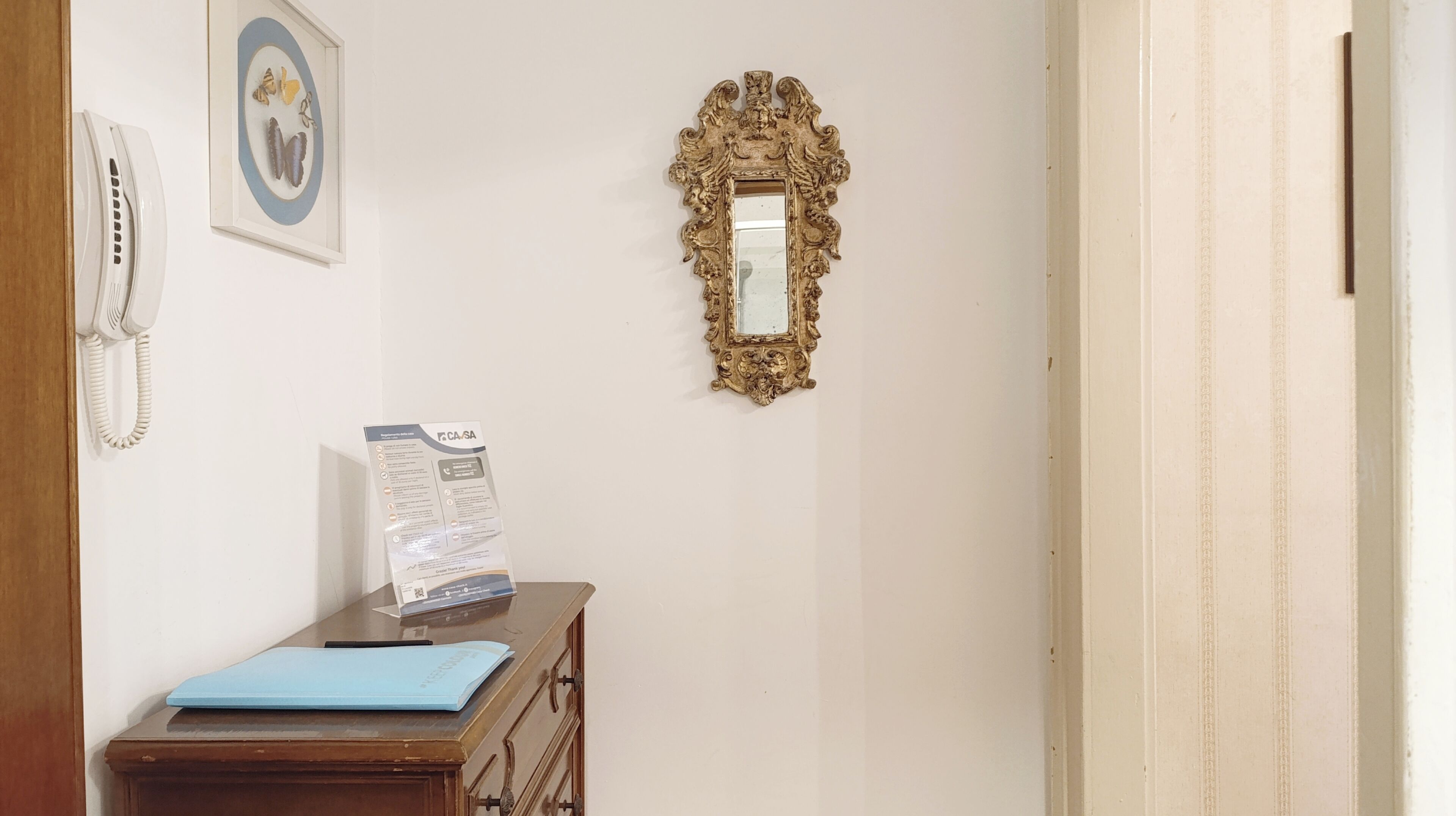 A room with a wooden desk, a framed mirror, a wall-mounted phone, and a framed picture.