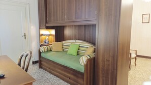 A compact room with a built-in sofa bed, a small table, and a lamp.