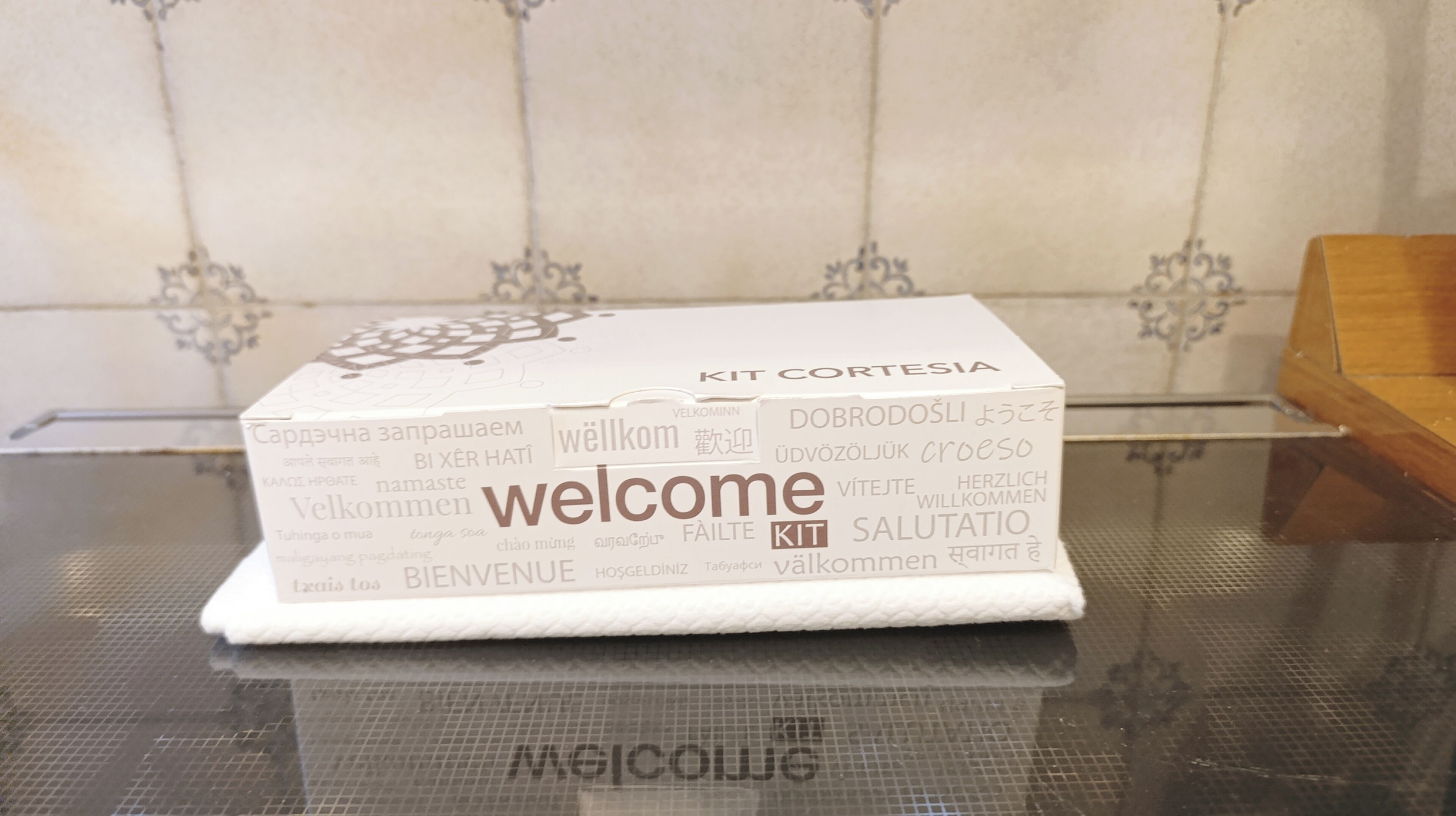 A white welcome kit box with multilingual text on its side, placed on a reflective surface.