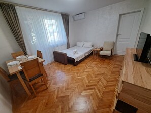 A small, tidy room with a bed, a chair, a table set for two, and a television. - Family Heritage from past to the future (Sibiu)