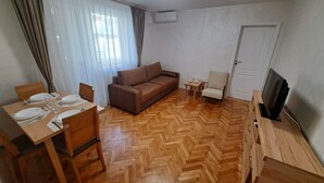 A furnished living room with a sofa, a dining table set for two, a TV stand, and a small table with cups. - Family Heritage from past to the future (Sibiu)