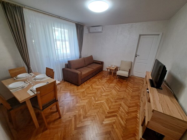 A furnished living room with a sofa, a dining table set for two, a TV stand, and a small table with cups. - Family Heritage from past to the future (Sibiu)