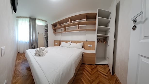 A bedroom with a bed, a built-in wardrobe, and a wooden floor. - Family Heritage from past to the future (Sibiu)