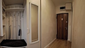 A narrow hallway with a wooden floor, a white wall with a door, and a bench with a black cushion. - Family Heritage from past to the future (Sibiu)