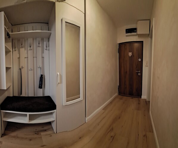 A narrow hallway with a wooden floor, a white wall with a door, and a bench with a black cushion.