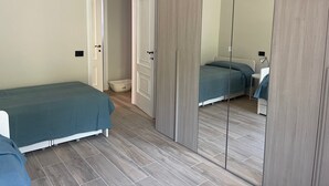 A bedroom with a bed, a small white table, a mirror, and a door leading to another room. - Oleandri cosy Apartment Near best beaches (Monterosso al Mare)