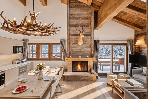 A spacious living area with a fireplace, a dining table set for four, and a large window overlooking a snowy landscape.