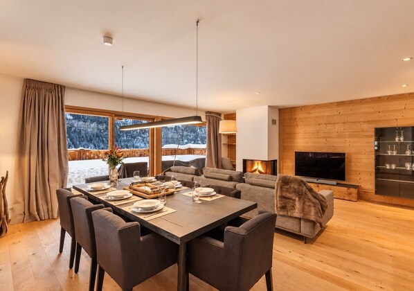 A modern living room with a wooden floor, a dining area with a table set for four, a sofa, and a fireplace.