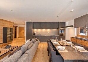 Una cocina moderna con una isla central, zona de comedor con una mesa larga y un rincón de estar acogedor con un sofá.