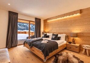 Un dormitorio con cama de madera, mesita de noche, lámpara y vistas a un paisaje nevado a través de la ventana.