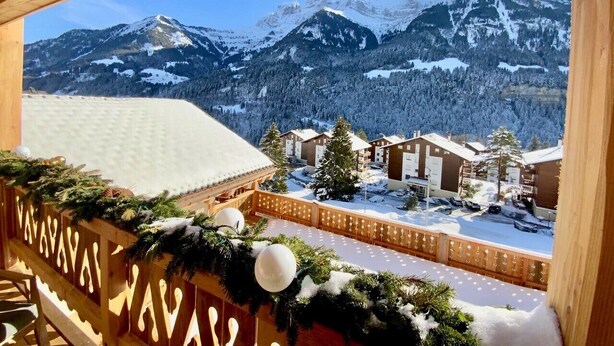 Un paysage montagneux enneigé avec un balcon en bois donnant sur une zone de villégiature.