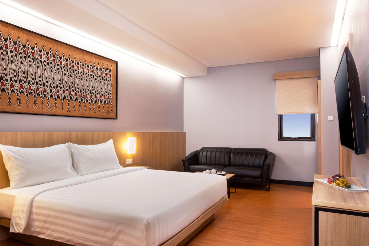 Une chambre d’hôtel comprenant un lit, un canapé en cuir noir, un téléviseur à écran plat et une œuvre d’art accrochée au mur.