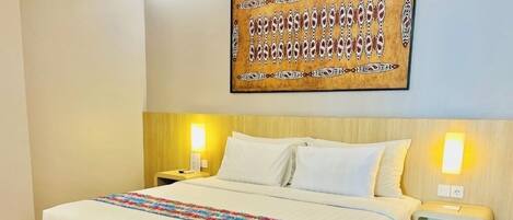 A hotel room with a large bed, wooden headboard, two bedside lamps, and a wall-mounted artwork.