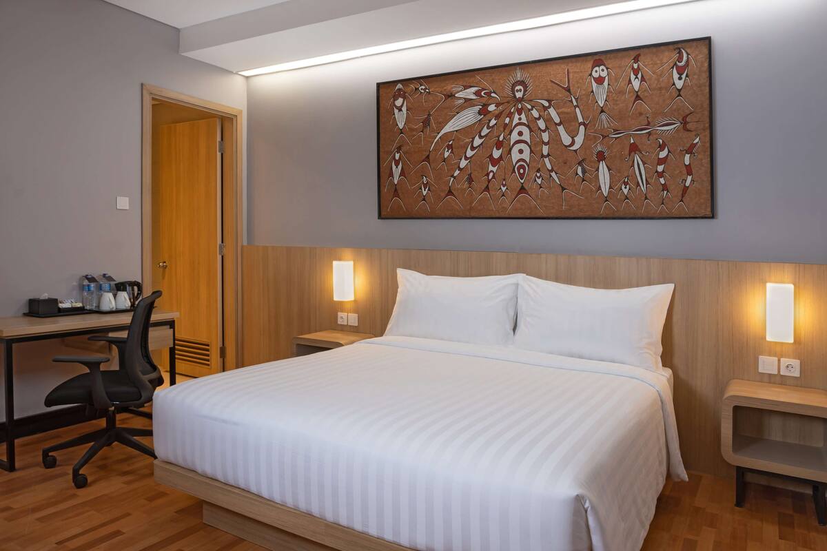 Ein Hotelzimmer mit Bett, Schreibtisch, Stuhl und einem Kunstwerk an der Wand.