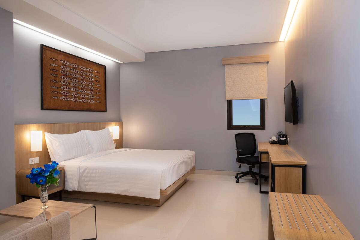 Ein modernes Hotelzimmer mit Bett, Nachttisch, Lampe und Schreibtisch mit Stuhl.