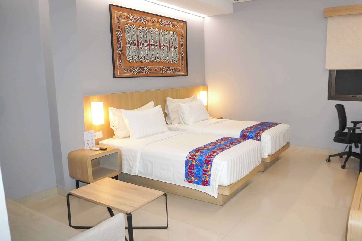 Ein Hotelzimmer mit zwei Betten, einem Schreibtisch, einem Stuhl, einem Fernseher und einem Wandbild.