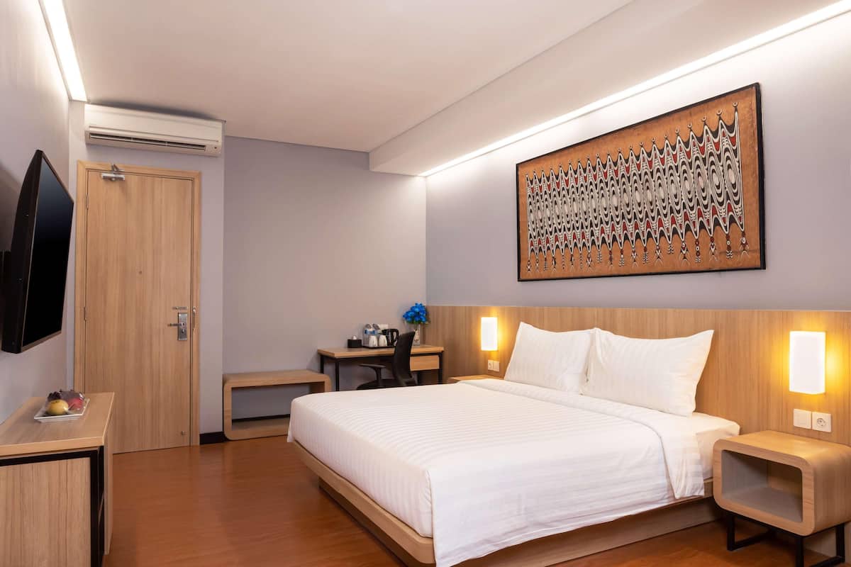 Une chambre d’hôtel équipée d’un lit, de tables de chevet, d’un bureau, d’un téléviseur à écran plat et d’une œuvre d’art accrochée au mur.