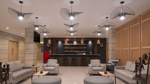 A modern living room with grey sofas, ottomans, and a bar area with stools. - Best Western Sagita Hotel Jayapura (Jayapura)