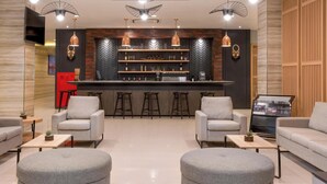 A modern lounge area with grey sofas, ottomans, and a bar with stools. - Best Western Sagita Hotel Jayapura (Jayapura)