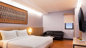 A hotel room with a large bed, a black leather sofa, a flat-screen TV, and a wall-mounted artwork. - Best Western Sagita Hotel Jayapura (Jayapura)