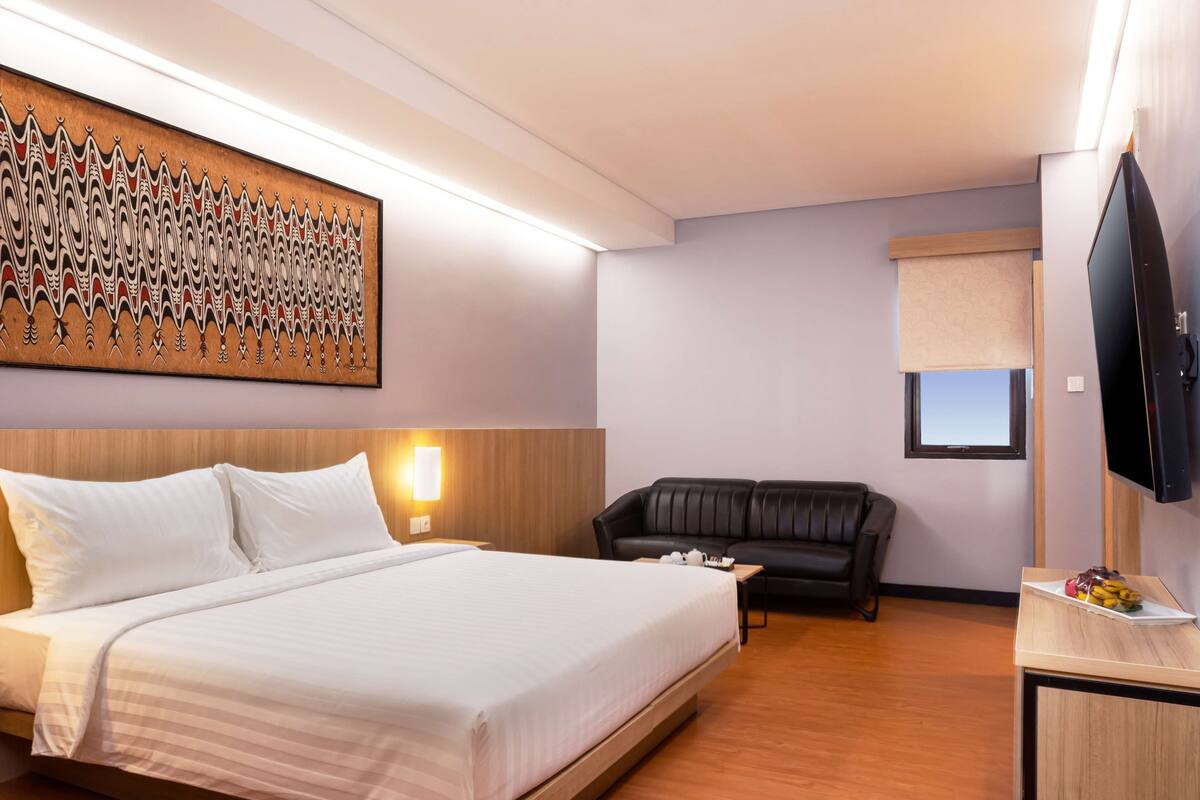 Ein Hotelzimmer mit einem großen Bett, einem schwarzen Ledersofa, einem Flachbildfernseher und einem Wandbild.