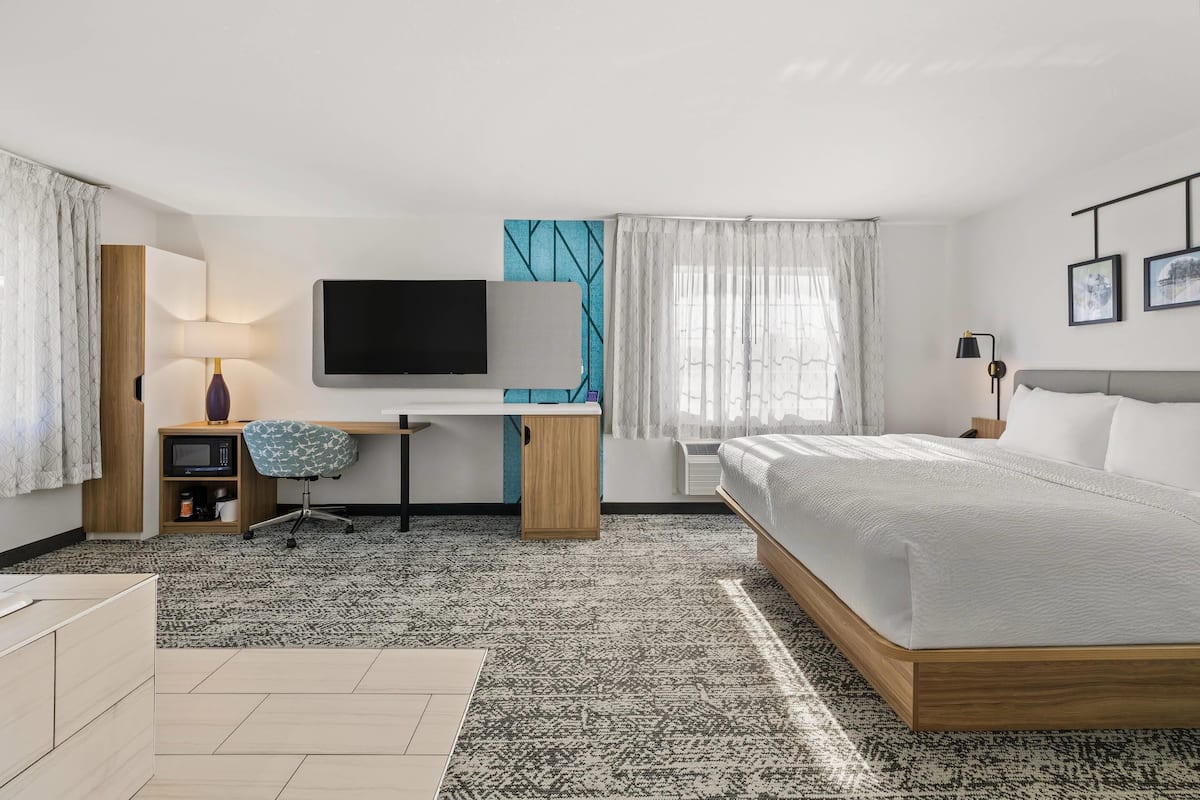 A modern hotel room with a bed, desk, TV, and a view of the city.