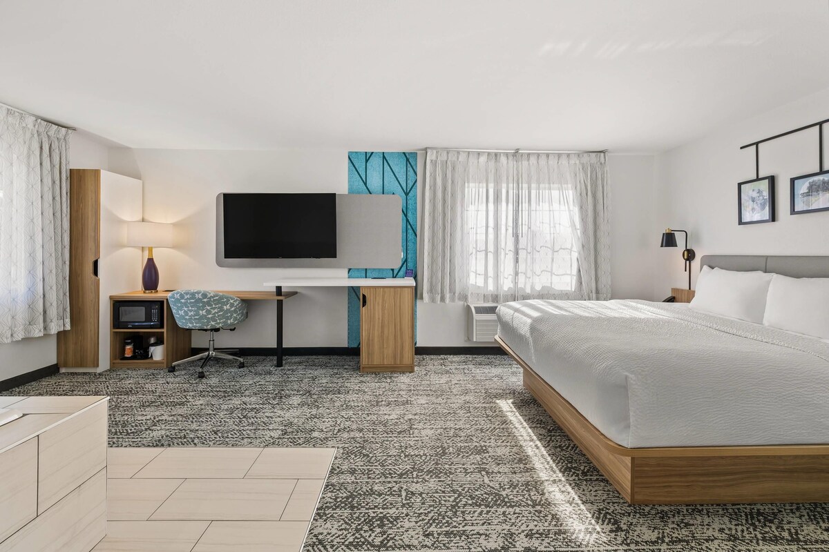 Habitación de hotel moderna con cama, escritorio, televisión y vistas a la ciudad.