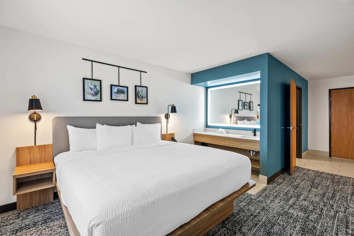 A hotel room with a large bed, bedside tables, a mirror, and framed pictures on the wall.