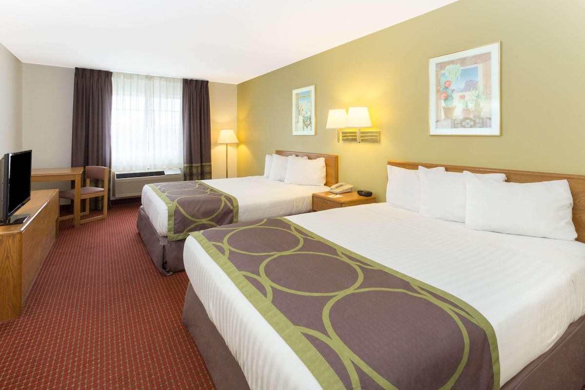A hotel room with two beds, a desk, a chair, a TV, and two wall-mounted lamps.