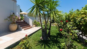 A well-maintained garden with a palm tree, a potted plant with red flowers, and a staircase leading to a white building. - Villa Filia in Prines (Rethymno)