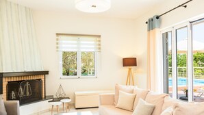 A living room with a fireplace, a sofa, a coffee table, and a view of a swimming pool. - Villa Filia in Prines (Rethymno)