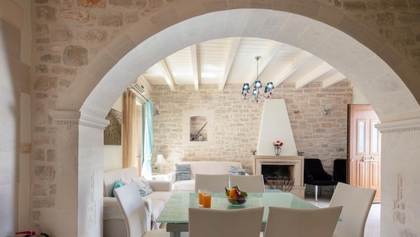 A stone-walled room with a high arched ceiling, a fireplace, and a dining area with a glass table and chairs. - Villa Katerina Dio in Asteri (Rethymno)