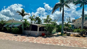 A building with a covered outdoor area, surrounded by palm trees and a paved walkway. - Turtle Nest Beach Studio (Fort Myers Beach)