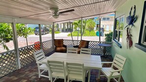 A covered outdoor seating area with a table and chairs, a ceiling fan, and a view of the street and buildings. - Turtle Nest Beach Studio (Fort Myers Beach)