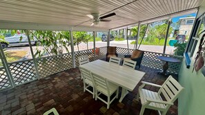 A covered patio area with a table and chairs, a ceiling fan, and a view of the street and greenery outside. - Turtle Nest Beach Studio (Fort Myers Beach)