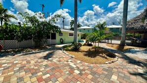 A paved courtyard with palm trees, a small building, and a thatched-roof structure. - Turtle Nest Beach Studio (Fort Myers Beach)