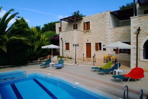A swimming pool with lounge chairs and umbrellas, surrounded by stone buildings with windows and doors.