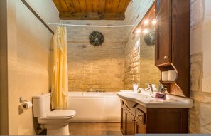 A bathroom with a stone wall, a bathtub, a toilet, and wooden cabinets.