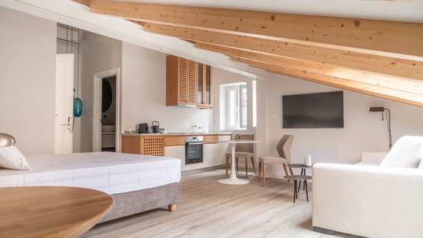 Et moderne soveværelse med træloft, en seng, en hvid sofa, et spisebord og et tekøkken.