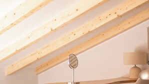 Et moderne loftværelse med synlige træbjælker, et rundt træbord, en lille orange skammel og en grå polstret stol.