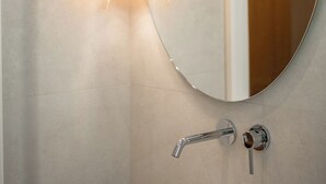 A bathroom with a round mirror, three hanging light fixtures, and a modern faucet.