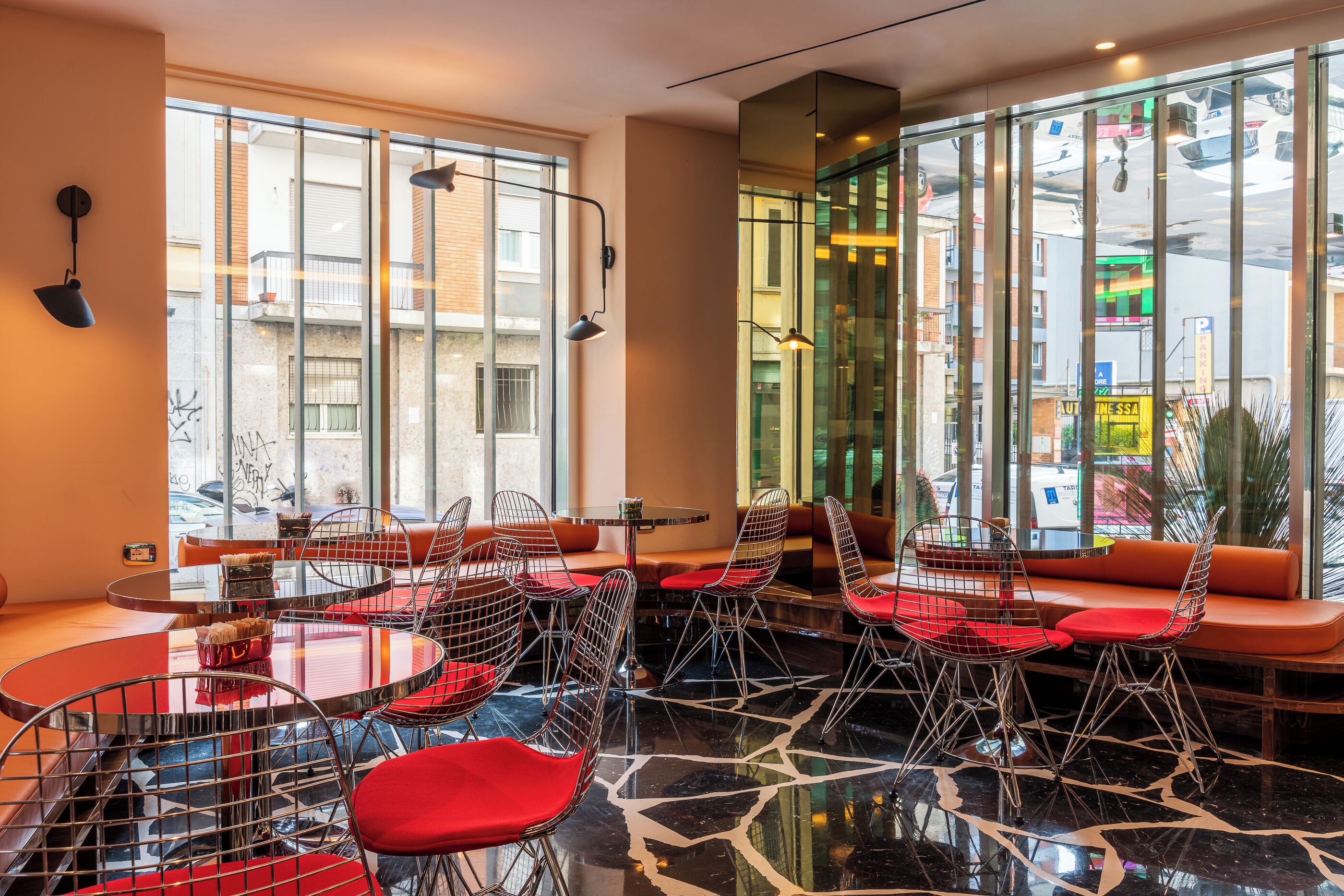 A modern interior with round tables and wireframe chairs, large windows, and a view of the street outside.