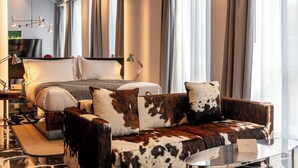 A modern hotel room with a large bed, a sofa with a cowhide pattern, a glass coffee table, and a large mirror reflecting the room. - Hotel Calimala Milano (Milan)