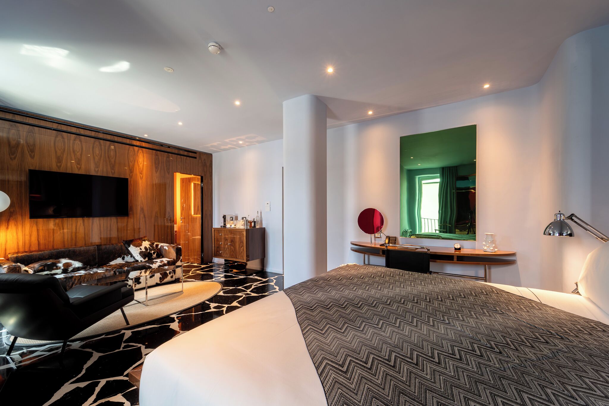 Ein modernes Hotelzimmer mit einem großen Bett, einer Couch, einem Schreibtisch und einem an der Wand befestigten Fernseher.