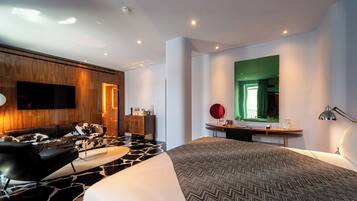 Ein modernes Hotelzimmer mit einem großen Bett, einer Couch, einem Schreibtisch und einem an der Wand befestigten Fernseher.