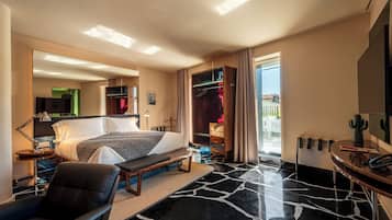 A modern hotel room with a bed, bedside table, chair, and a desk with a telephone.